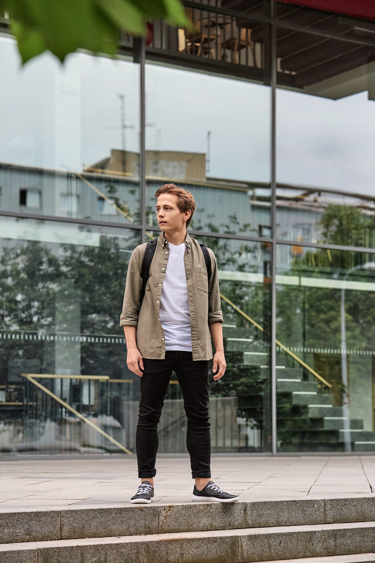 Mand med sorte sneakers står foran moderne glasfacade