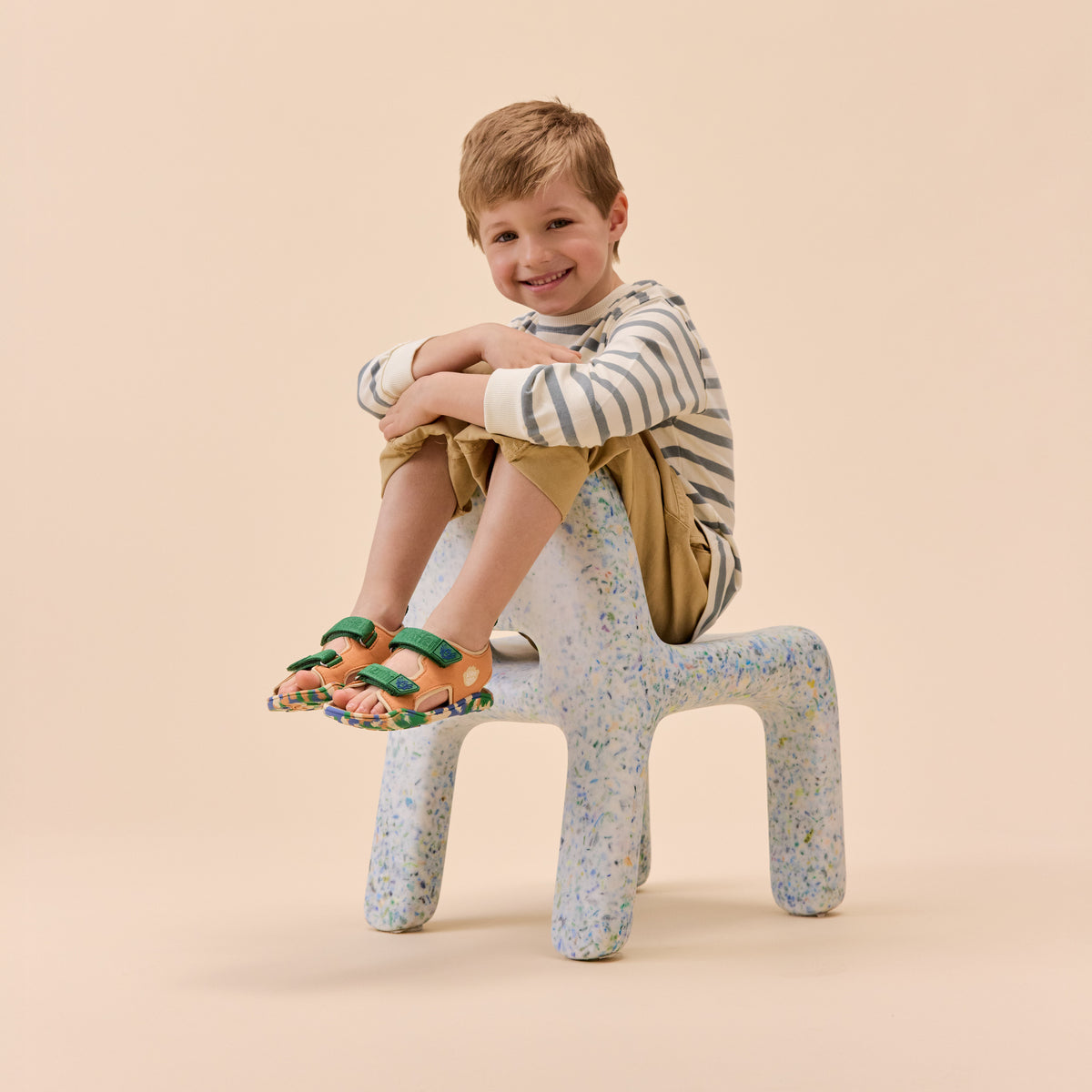 Enfant souriant assis sur une chaise avec les sandales aux pieds