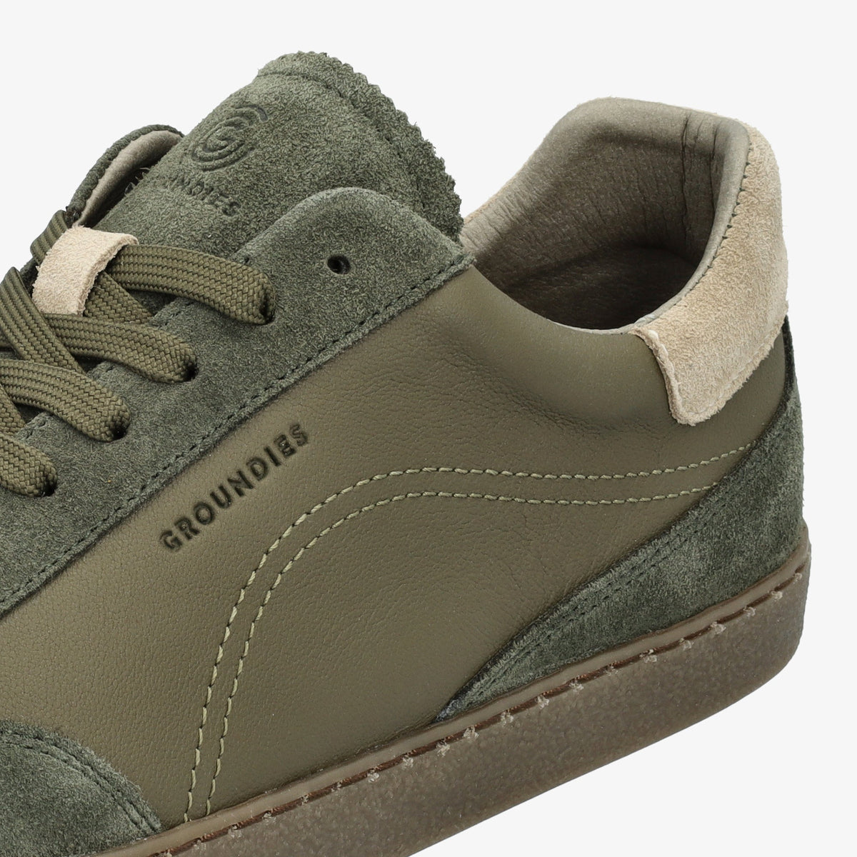 Nærbillede af syninger, glat læder og ruskind ved hælen på khaki sneaker