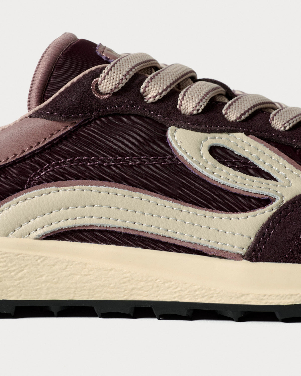 Nærbillede af snørebånd, syninger og cremefarvede paneler på bordeaux sneaker