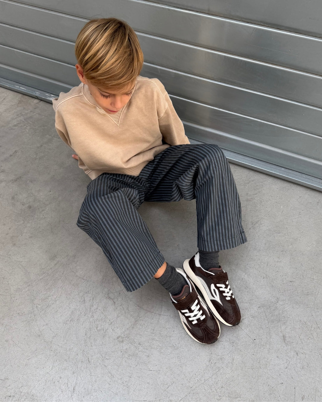 Brune børnesneakers på fod hos dreng, der sidder på betongulv