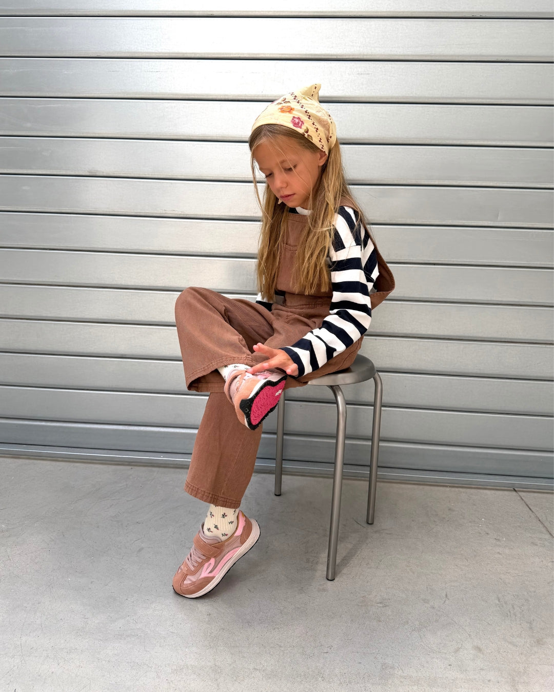 Barn på skammel med rosa børnesneakers på fødderne foran grå rulleport