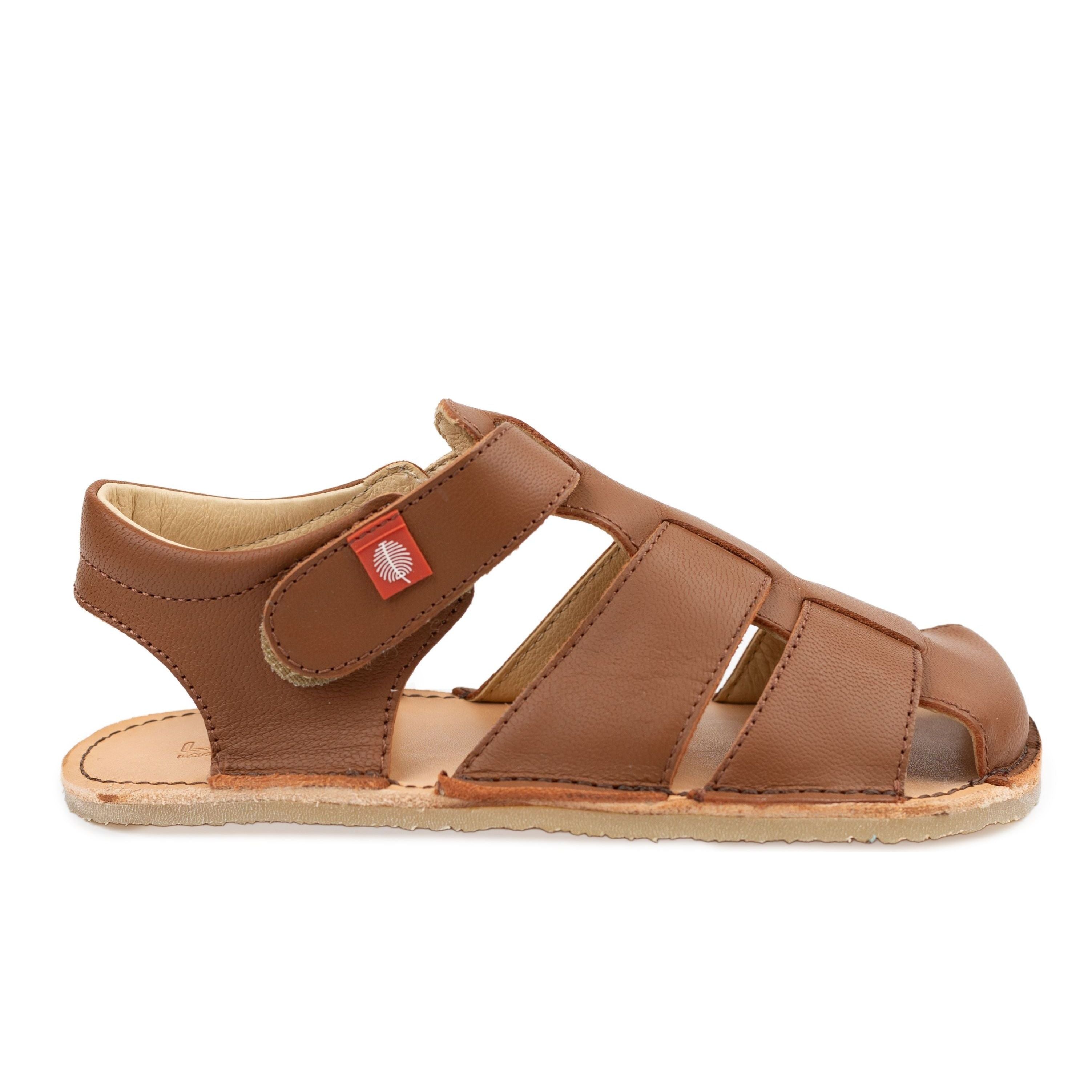 Tikki Lasta Leather sandal i Bruno variant for børn, lavet af brunt læder med stropper og en tynd sål til en barfodet følelse. Hook-and-loop lukning med rødt mærke.