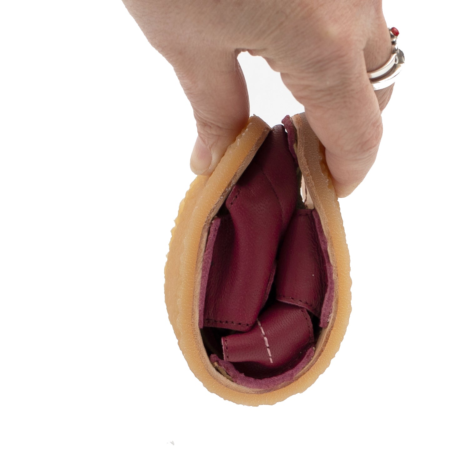 Fleksibel børnesko fra Tikki, Lasta Leather Farfalla, i dyb bordeaux læder med lys tan sål, holdt i en hånd for at vise den bøjelige, minimalistiske stil.