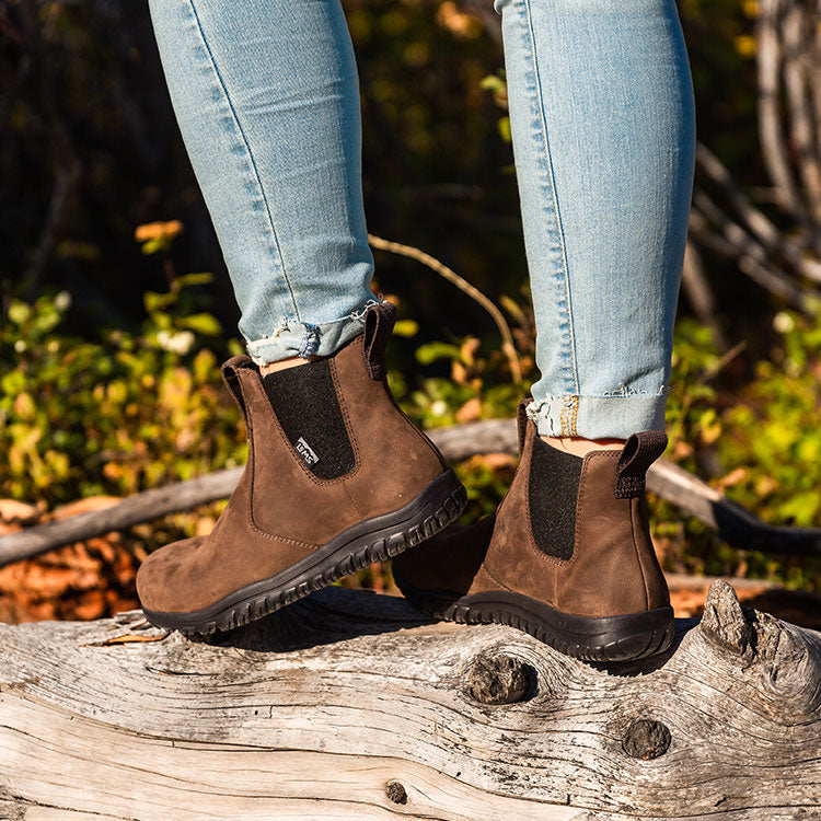 Unisex Lems Chelsea Boot Waterproof in Espresso on model outdoors. Brown with black elastic sides and rugged sole, perfect for nature walks. Shows style and functionality.