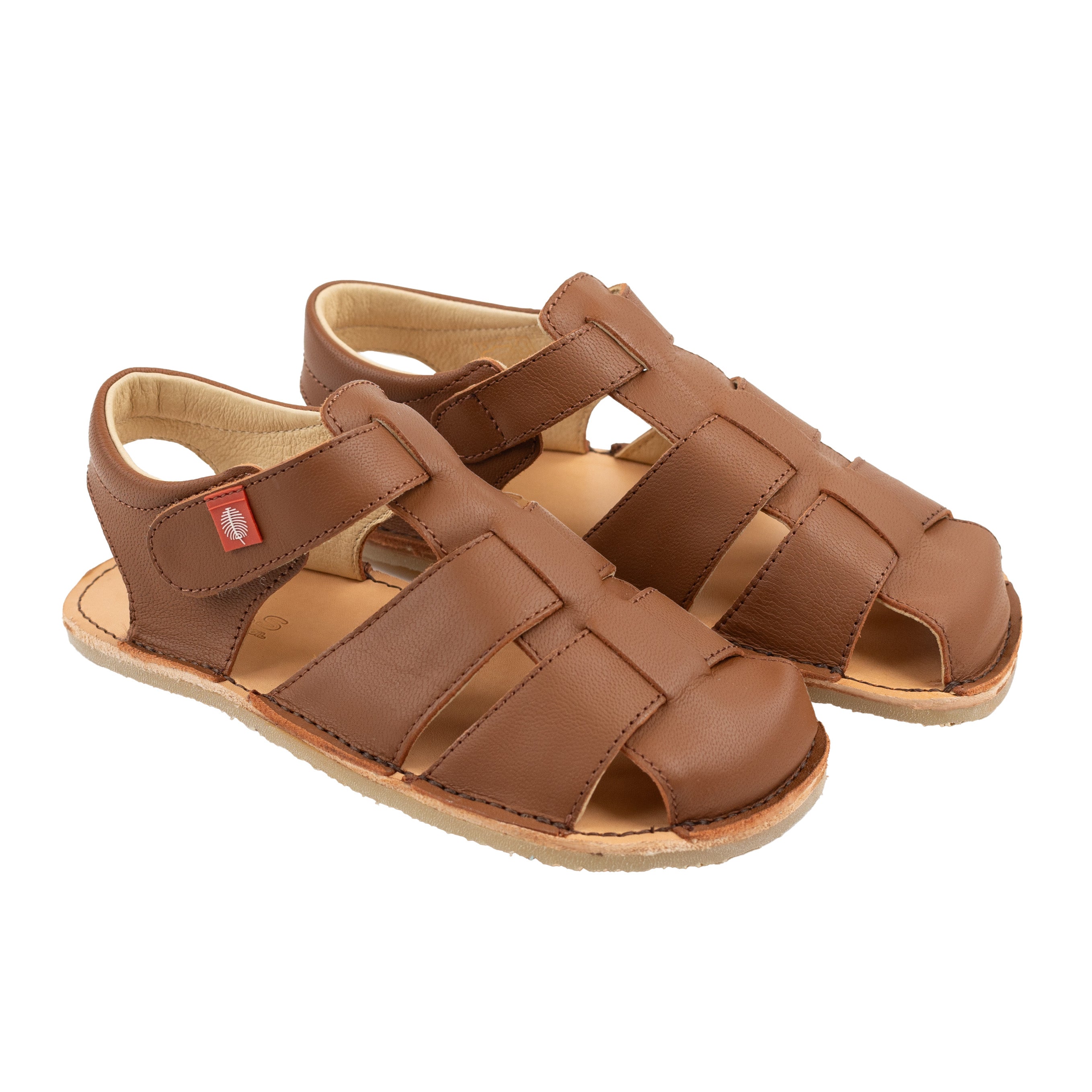 Tikki Lasta Leather sandaler, Bruno variant, til børn. Lavet af brunt læder med flettede remme og lukket tå, designet til en barfodsfølelse. Blød, beige foring for komfort.