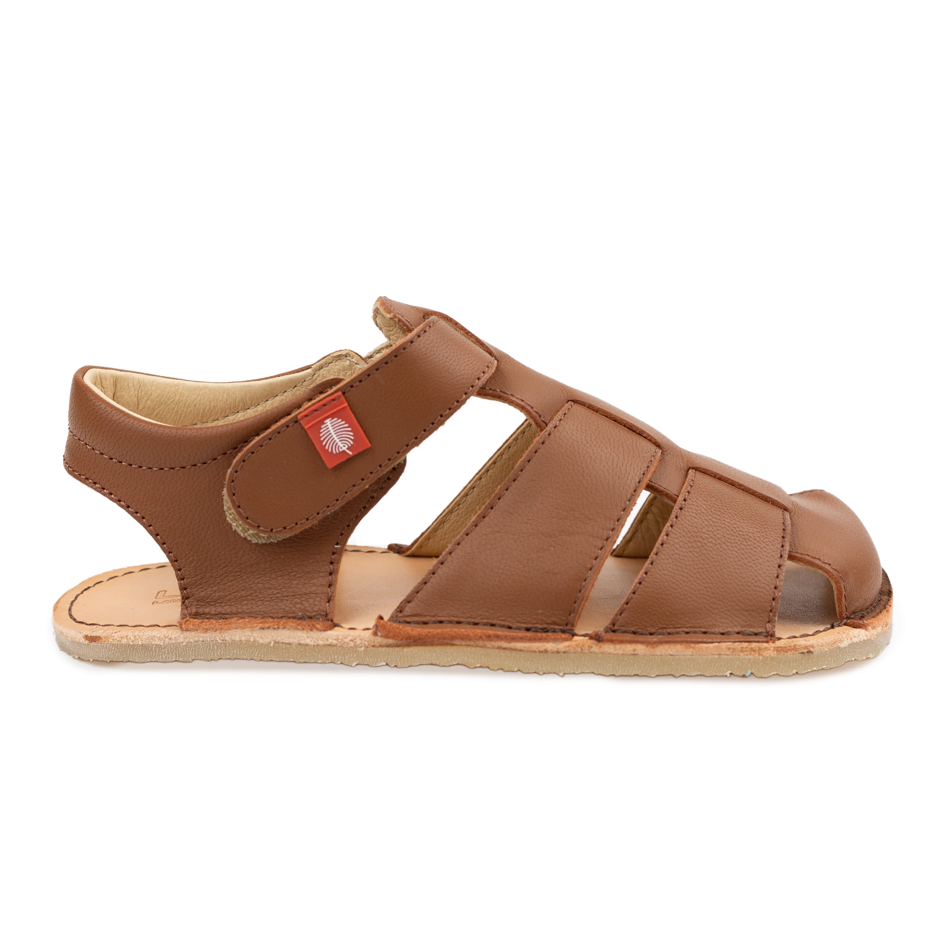 Tikki Lasta Leather sandal i Bruno variant for børn, lavet af brunt læder med stropper og en tynd sål til en barfodet følelse. Hook-and-loop lukning med rødt mærke.