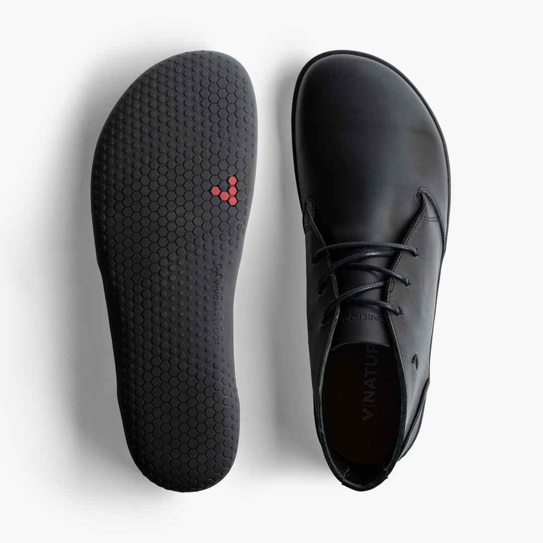 Vivobarefoot Gobi Lux model Obsidian, barfodssko til mænd, viser både overlæder og ydersåls design. Skoen fremhæver en glat sort læderoverdel og en hexagonal gummisål med røde detaljer for bedre greb.