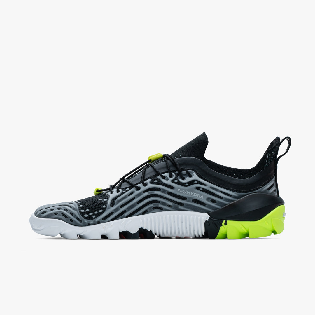 Vivobarefoot Hydra ESC Womens sko i Obsidian / Safety Yellow vises fra siden indvendig. Barfodet design, sort mesh med grå bølgede overlays, hurtigsnor og Michelin-sål med gult.