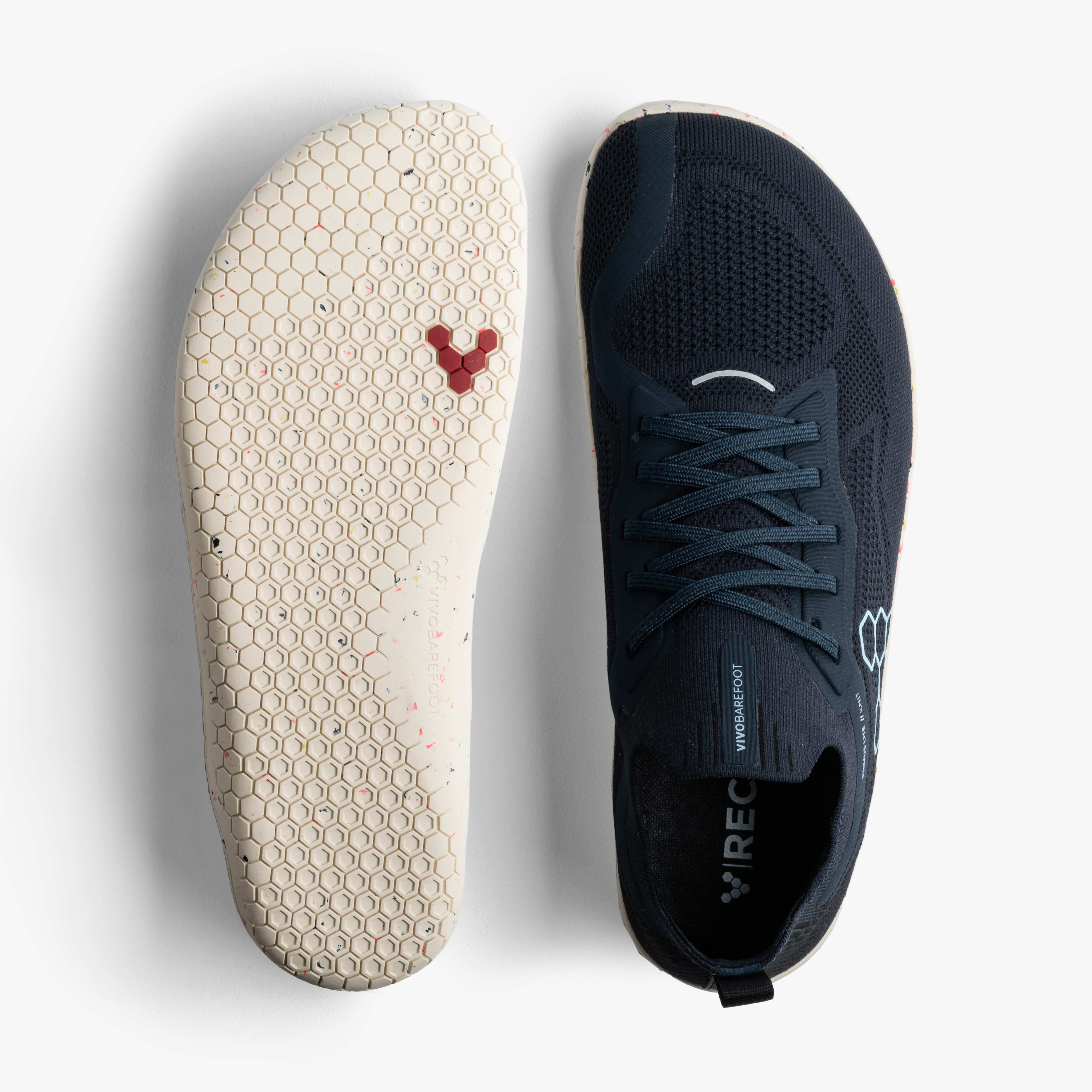 Vivobarefoot Primus Lite Knit Mens i varianten Midnight, viser både top- og sålperspektiv. Sneakeren fremhæver en fleksibel og åndbar mørkeblå strikket overdel og en ultratynd creme-farvet sål med hexagonal mønster for naturlig fodbevægelse.