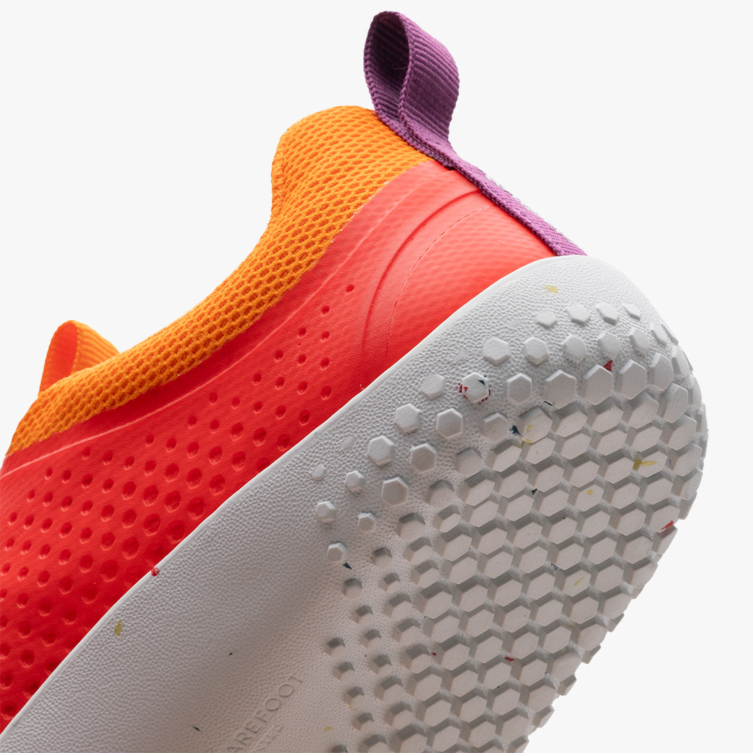 Nærbillede af Vivobarefoot Primus Sport III Juniors sko i Cherry Tomato, viser lilla hæltræk, orange mesh og hvid sål med sekskantet mønster. Ideel til barfodsfleksibilitet.