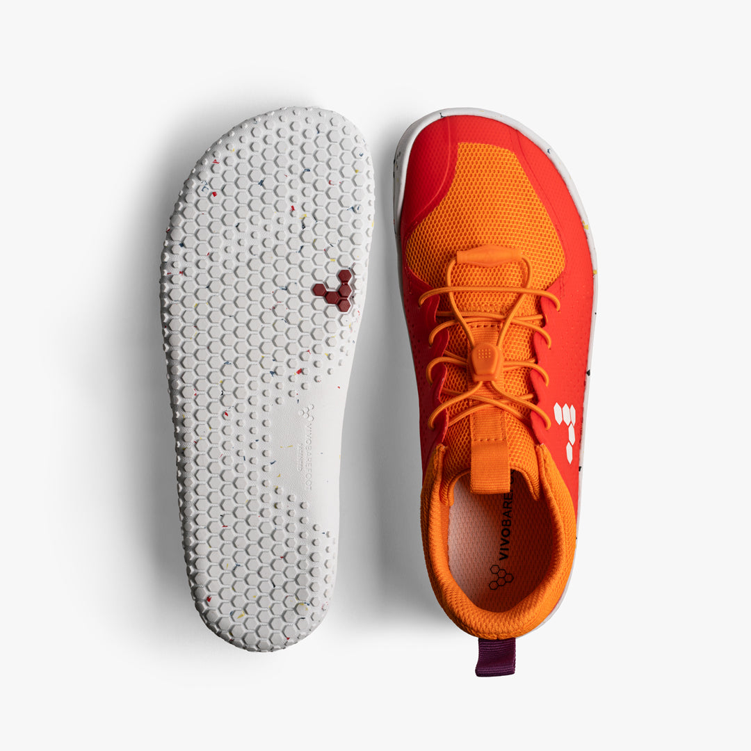 Vivobarefoot Primus Sport III Juniors i Cherry Tomato. En sko set fra toppen, viser orangerød mesh med snørebånd og Vivobarefoot logo. Sål med hvidt gummi og mønster af små farvepletter.