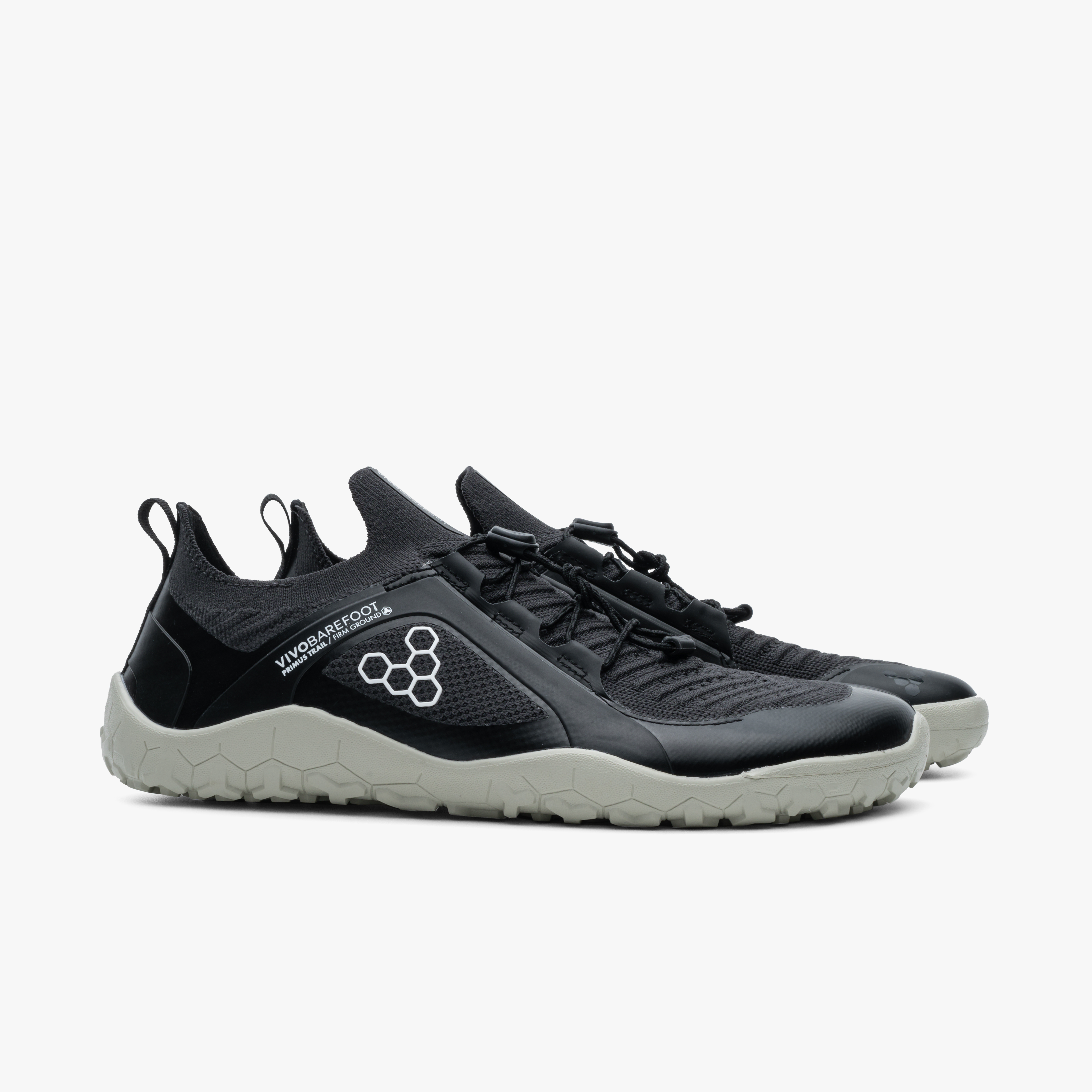 Vivobarefoot Primus Trail Knit FG i farverne Obsidian / Pelican, viser et par letvægts barfodssko til mænd. Skoene har åndbar mesh øverst og hexagonal logo på siden. Ideelle til trail løb.