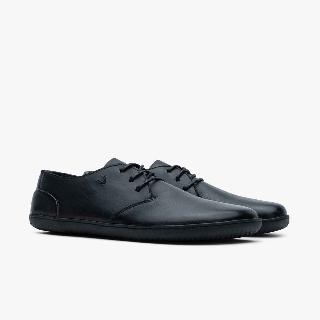 Vivobarefoot Ra III Lux Mens sko, Obsidian variant, i glat, metal-frit læder med sorte snørebånd. Minimalistisk design med lav-profil gummisål, set fra en vinklet perspektiv.