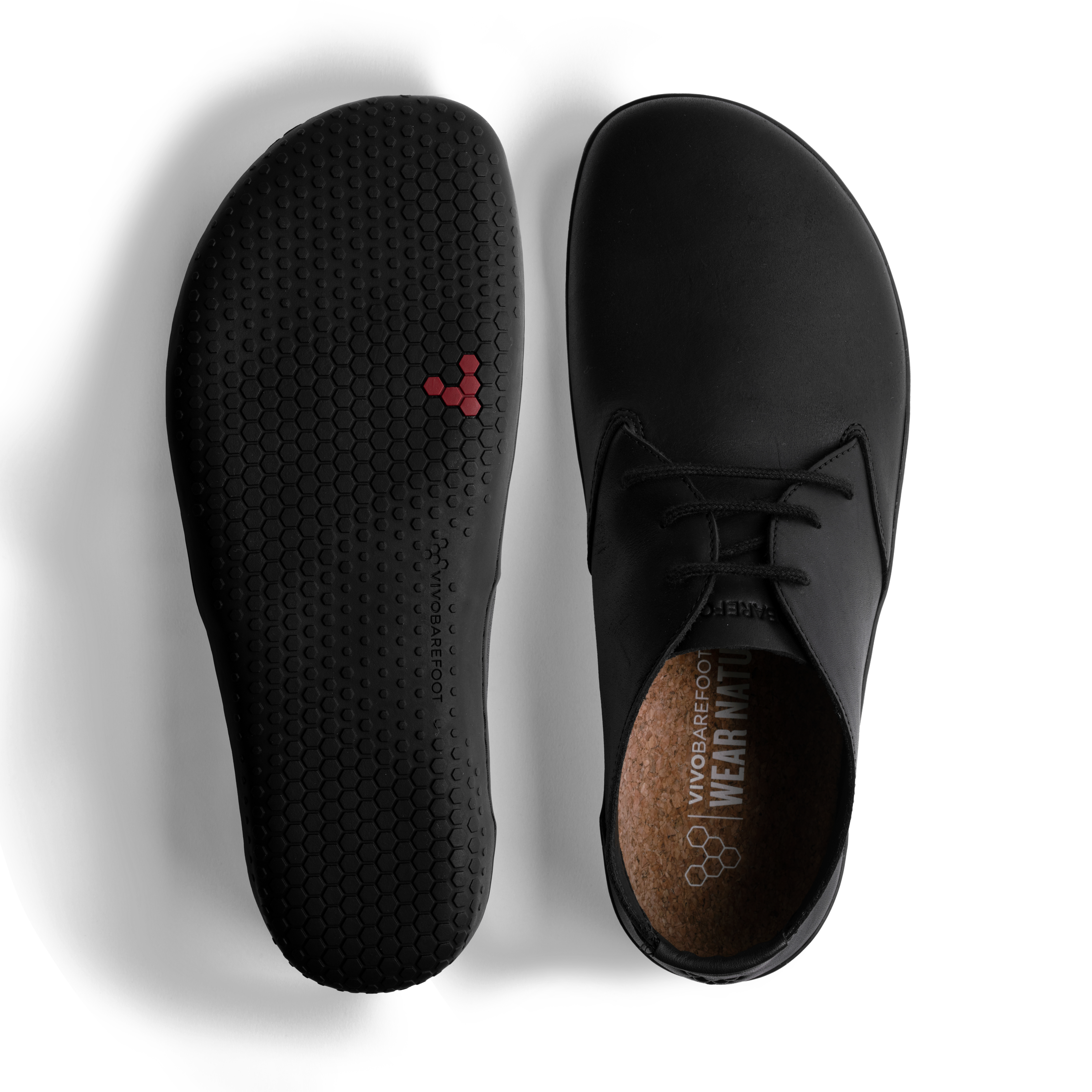 Par af Vivobarefoot Ra IV herresko, variant Obsidian, med synlig korkindersål og fleksibel sort ydersål med sekskantet mønster. Skoen kombinerer naturlig fodbevægelse og bæredygtige materialer.