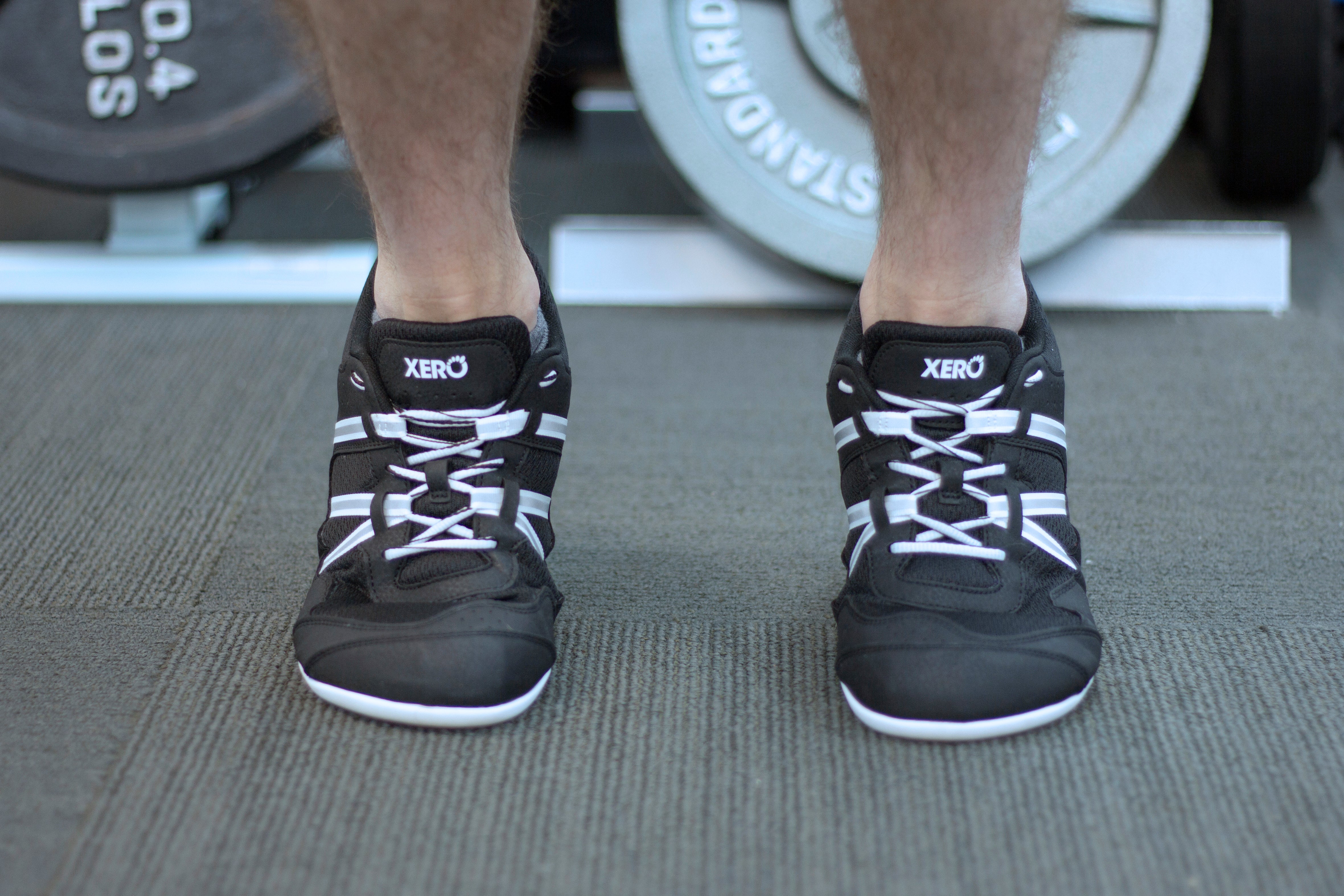 Xero Shoes Prio Men in Black/White worn by a model, highlighting barefoot design and reflective straps for versatile fitness and everyday wear.