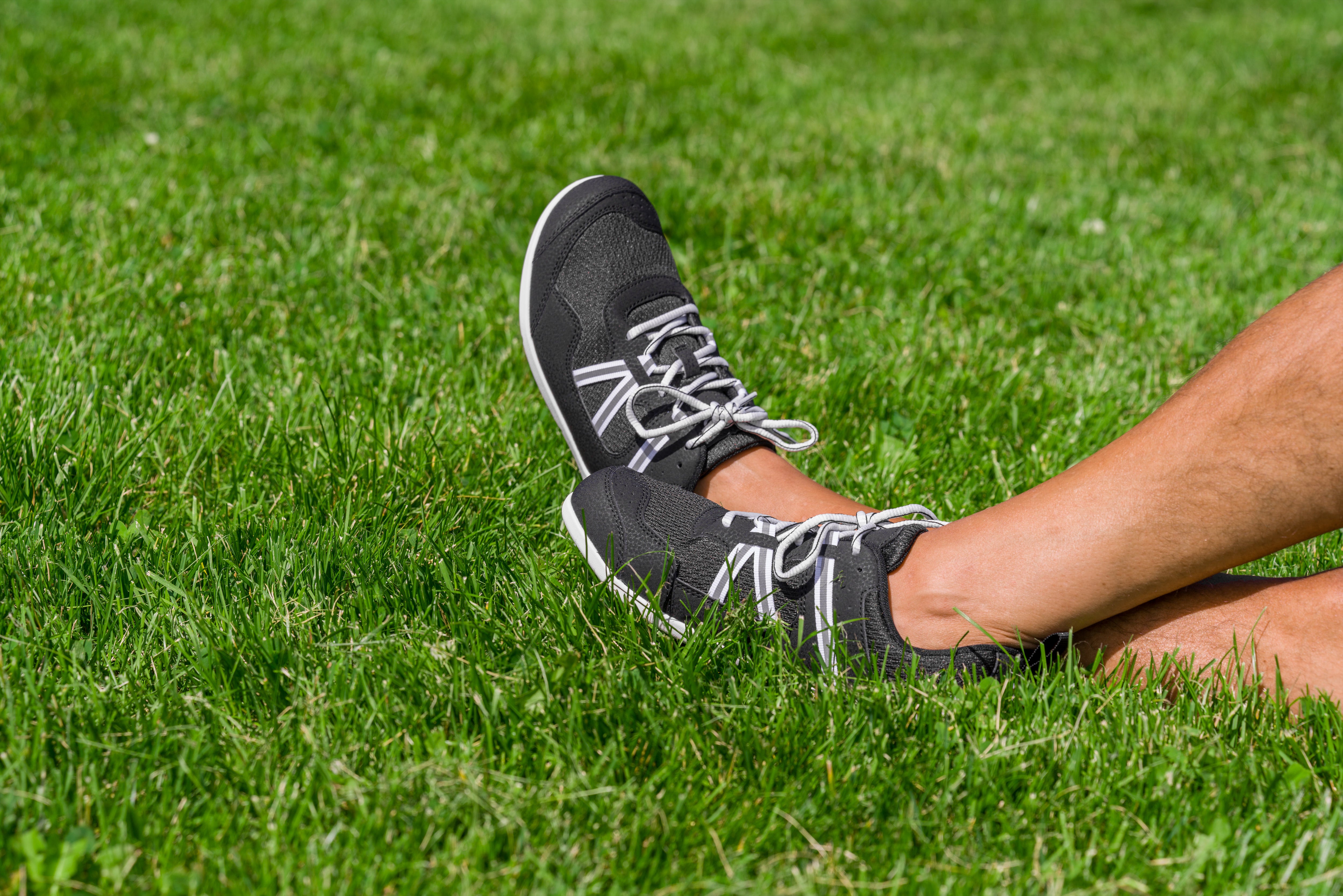 Xero Shoes Prio Men Black/White barefoot shoes worn outdoors on grass, showing flexible design and natural fit with black mesh and white accents.